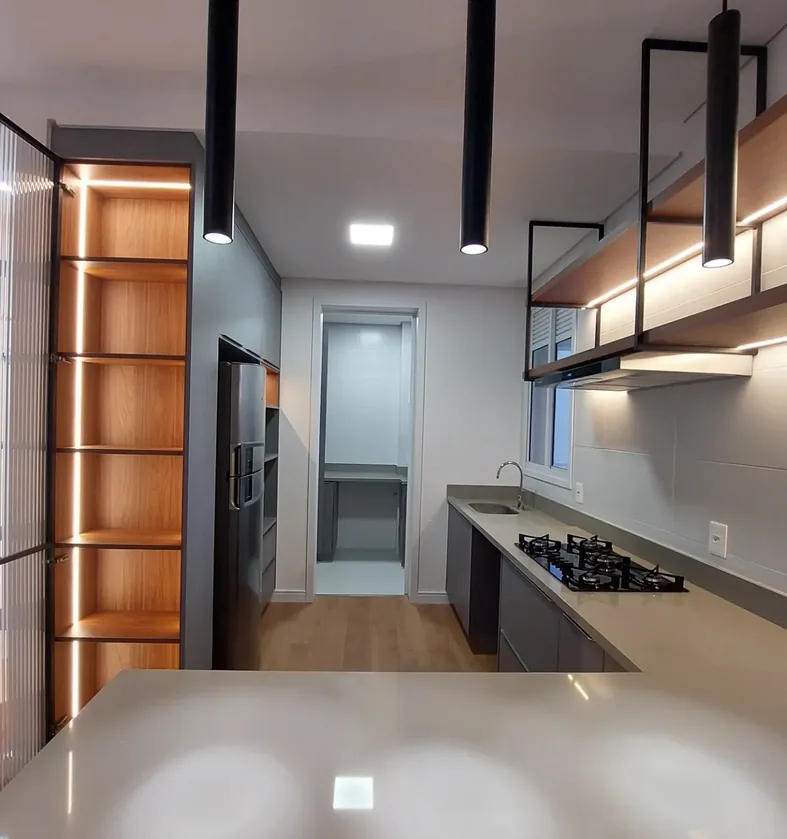 Cozinha em tons de cinza com prateleiras suspensas de estrutura metálica, cristaleira iluminada por LED e pendentes pretos