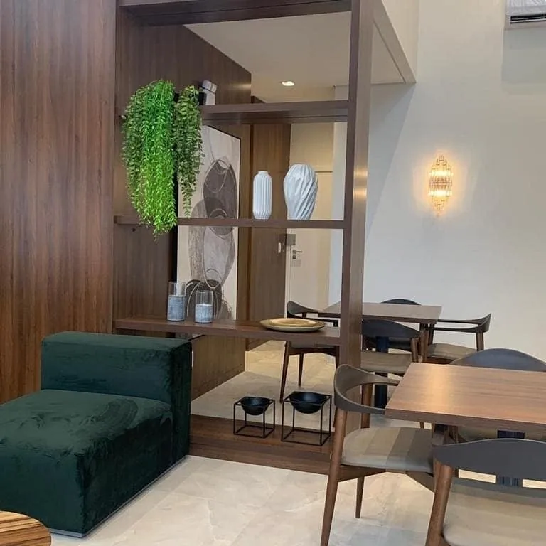 Ambiente corporativo com estante divisória vazada amadeirada, painel amadeirado escuro, sofá de veludo verde e mesas com cadeiras